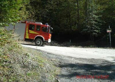 Ein Feuerwehr LKW fährt einen Seinbruch Runter auf einer Kiesstraße um die Kurve rum, im Hintergrund ein paar Bäume die den Hang hinauf gehen beim Schadenpräventionstraining