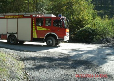 Ein Feuerwehr LKW fährt einen Seinbruch Runter auf einer Kiesstraße um die Kurve rum, im Hintergrund ein paar Bäume die den Hang hinauf gehen beim Schadenpräventionstraining