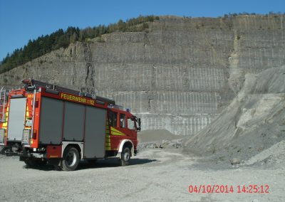 Ein Feuerwehr LKW steht in einen Steinbruch , im Hintergrund hohe Steinwände die hinauf gehen beim Schadenpräventionstraining