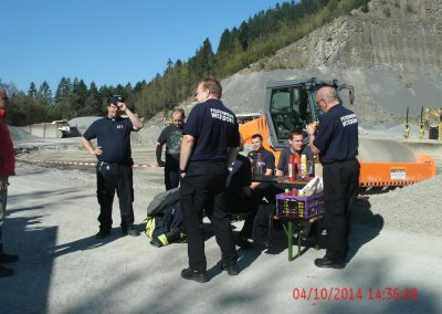 Mittag im Steinbruch die Feuerwehr Mitarbeiter stehen im Steinbruch und essen an einem Picknicktisch was zum Mittag Im Hintergrund ein Bagger