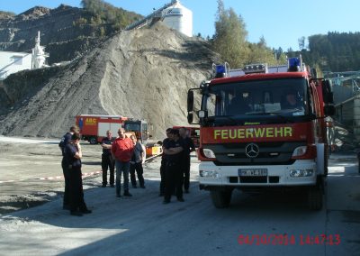 bei der Ablaufbesprechung stehen die Feuerwehr Mitarbeiter neben dem einsatz fahrzeug und besprechen sich im Hintergrund ein berg aus schutt und förderbänder