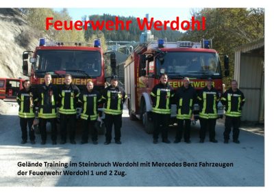 Gruppenfoto der Feuerwehr Werdohl vor den zwei Feuerwehr Fahrzeugen stehen die neun feuerwehr männer in einer Reihe. Im Hintergrund sieht man den wald und einen Teil des Steinbruches